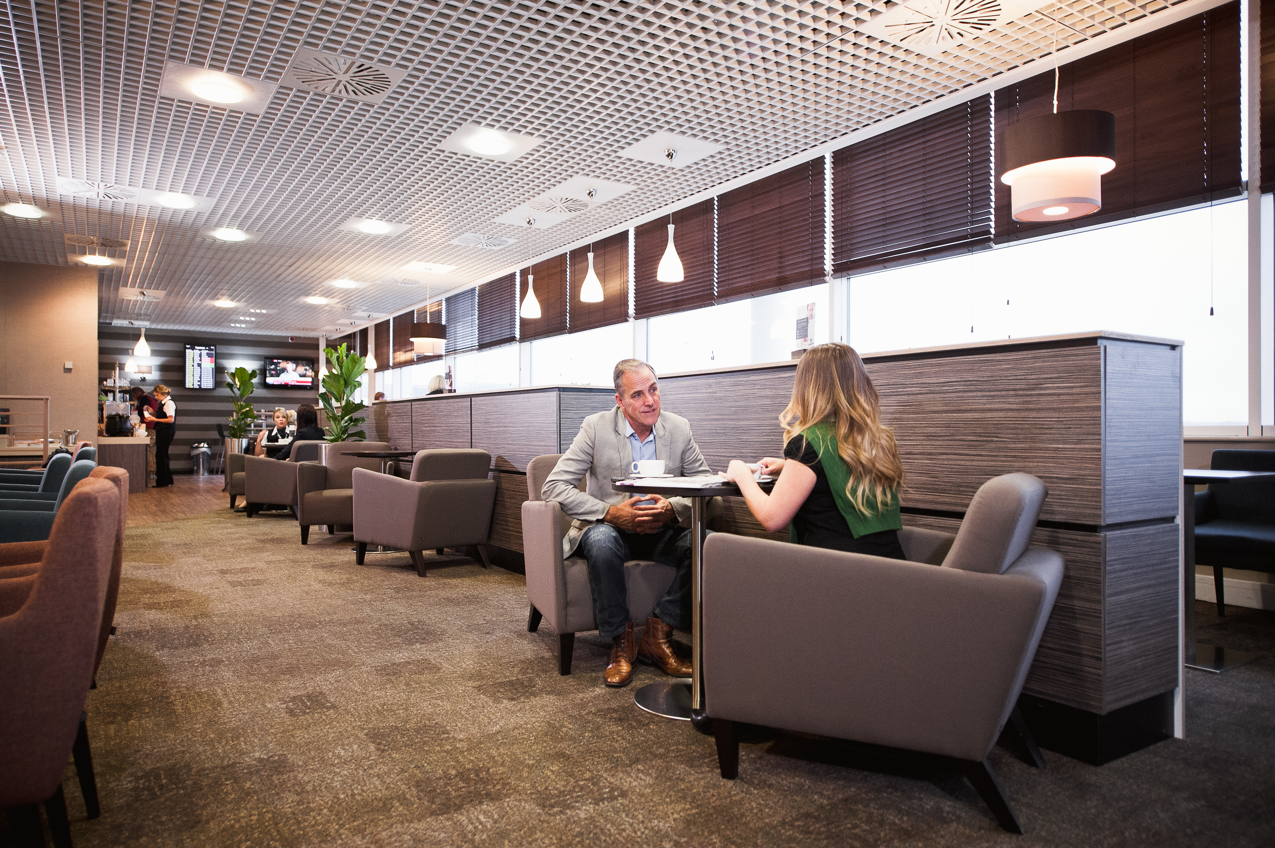 Two travellers socialising in comfortable armchairs in the Birmingham Aspire Lounge.