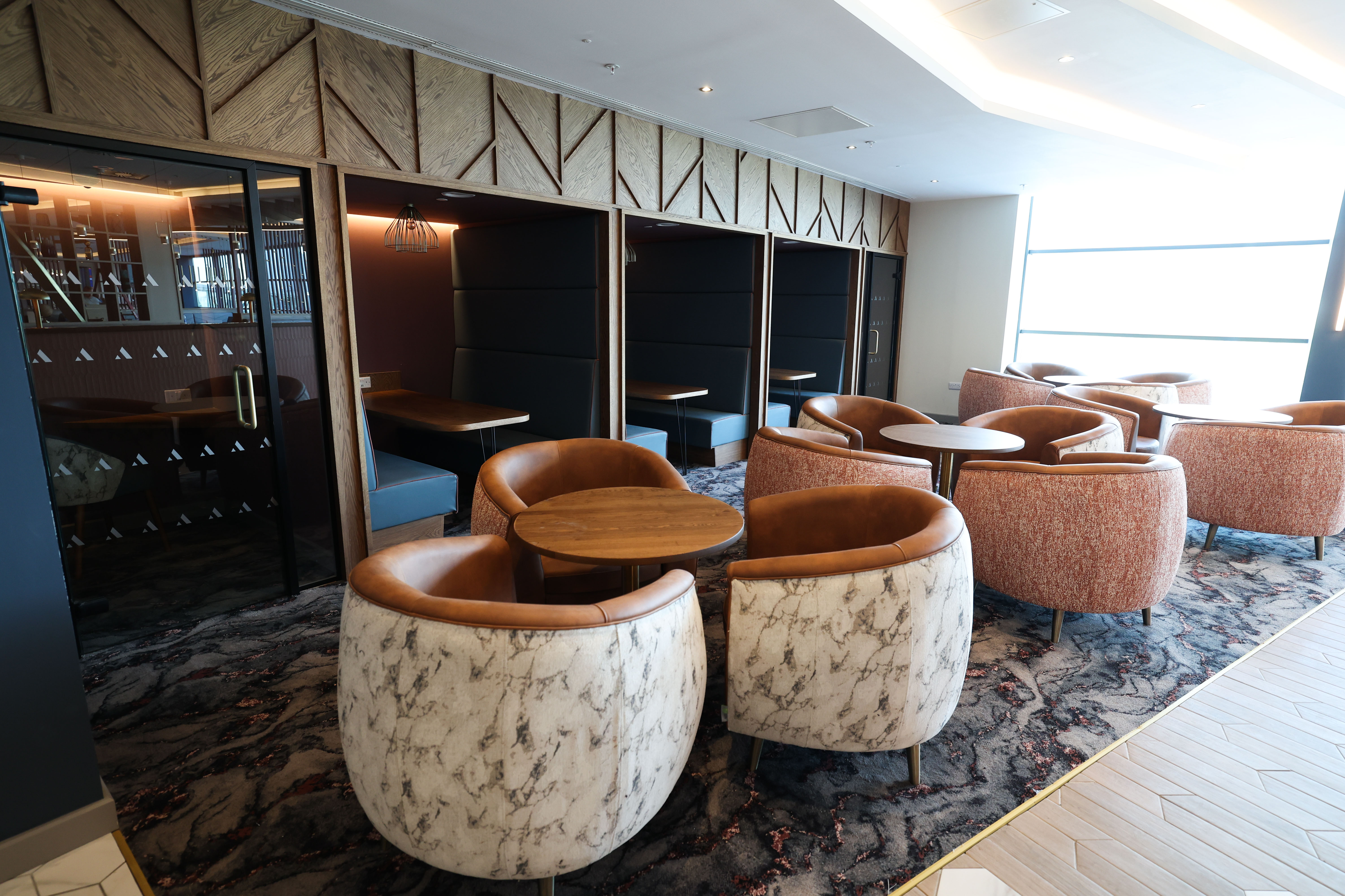 Modern lounge seating with upholstered club chairs and round tables in the Belfast Aspire Lounge.